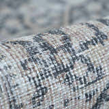 Close-up of the textured weave of a rolled Hedda Boutique Washable Rug in dark gray, gray, and nutmeg. Fold