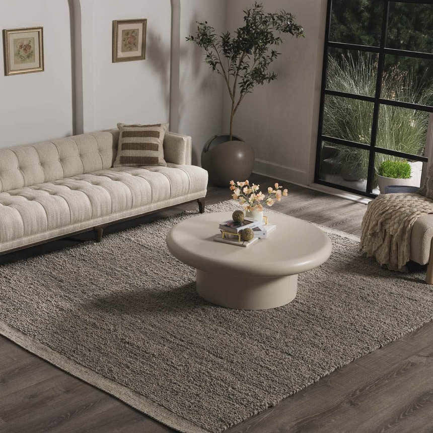 Living room scene with a charcoal Basiao Area Rug, beige sofa, round coffee table, and dark wood floors. Roomscene-Rectangle