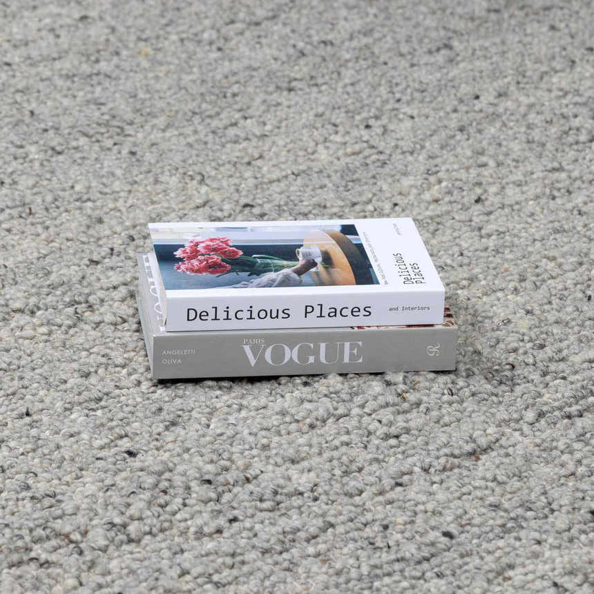 Close-up of the hand-woven Basiao Area Rug showing charcoal, cream, and gray tones. Stack of books on the rug. Styleshot