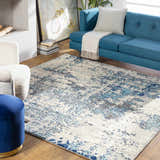 Living room scene with a Beverly Abstract Blue Area Rug, blue sofa, and cream armchair. Roomscene-Square