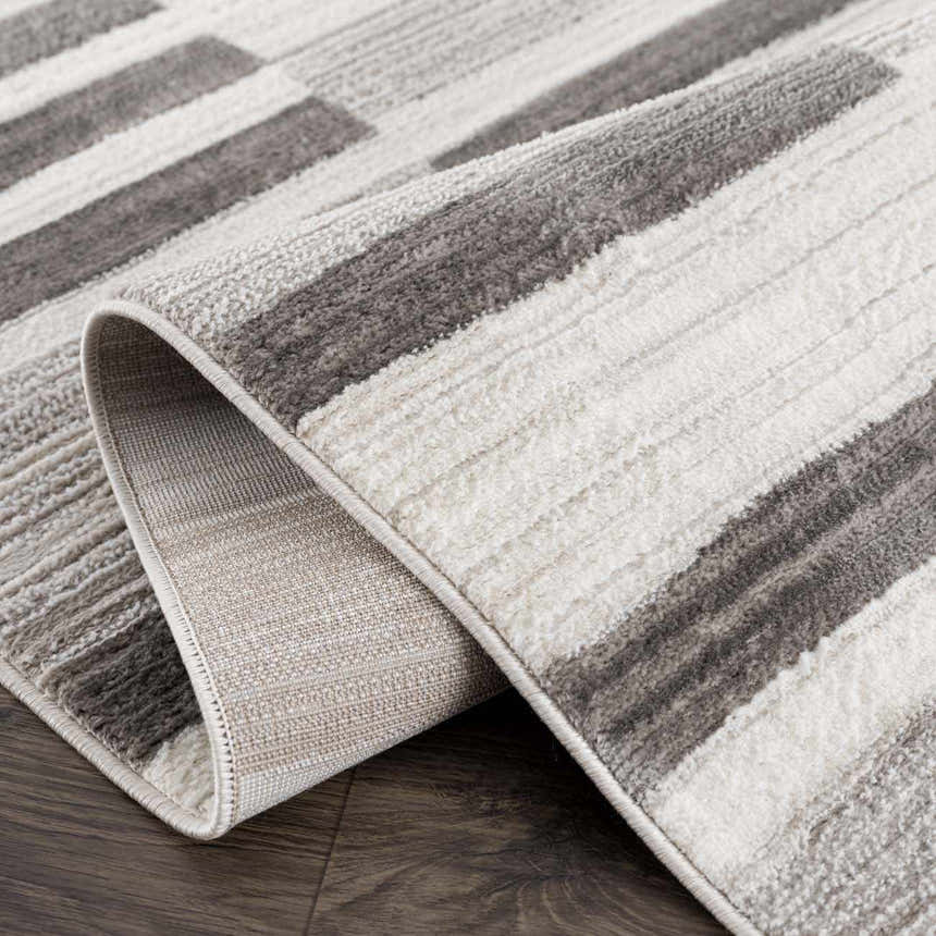 Close-up of the Bojana Broken-Striped Area Rug. Geometric design in black, cream, off-white, and vizon. Machine woven texture. Fold