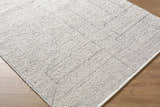 Close-up of the hand woven Brenta Area Rug. Gray, light silver, and sage hues with a subtle geometric pattern. Corner