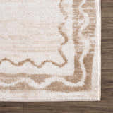 Close-up of the Beatus Washable Area Rug. Beige rug with a light brown geometric pattern and border on dark wood floor. Corner