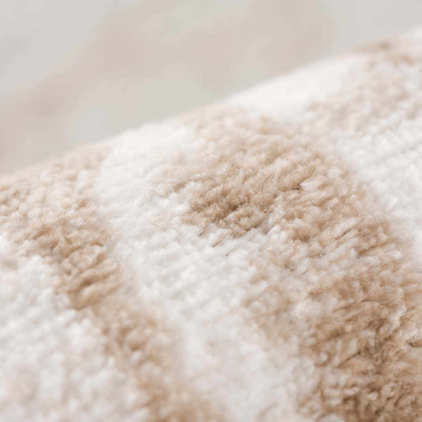 Close-up of the Beatus Washable Area Rug. Beige and light brown geometric pattern. Soft, textured polyester rug. Fold