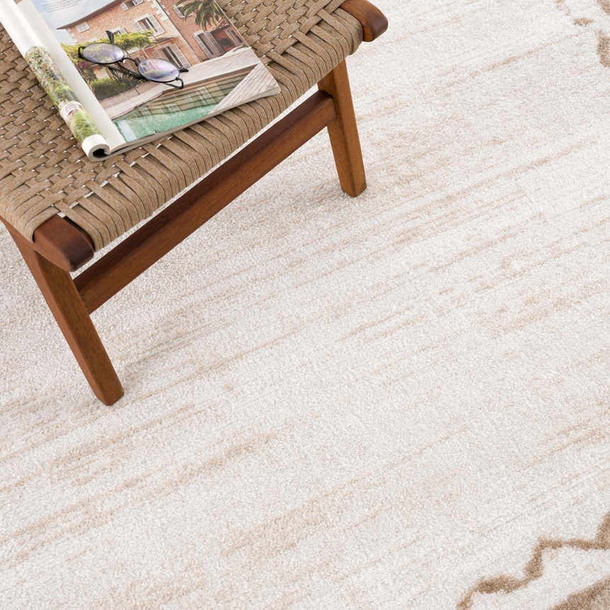 Close-up of the beige and light brown geometric Beatus Washable Area Rug with a woven stool and magazine. Styleshot