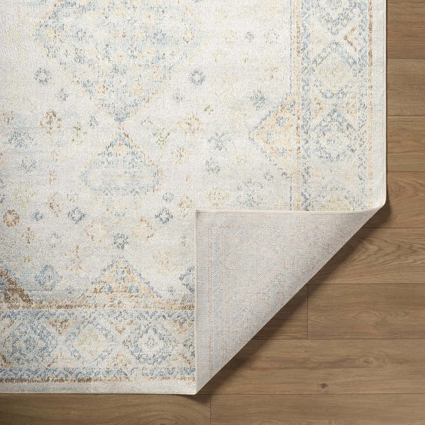 Close-up of the Bhavya Cream Washable Area Rug showing its beige, muted blue, and sage traditional pattern and non-slip backing. Fold