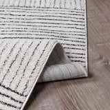 Close up of Modern Scandi High Pile Architect I Area Rug. Ivory rug with black stripes shows texture and backing. Fold