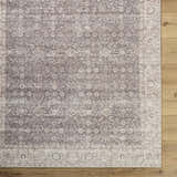 Close-up of Spokane Machine Woven rug. Beige, cream, and brown traditional pattern with a detailed border on wood floors. Corner