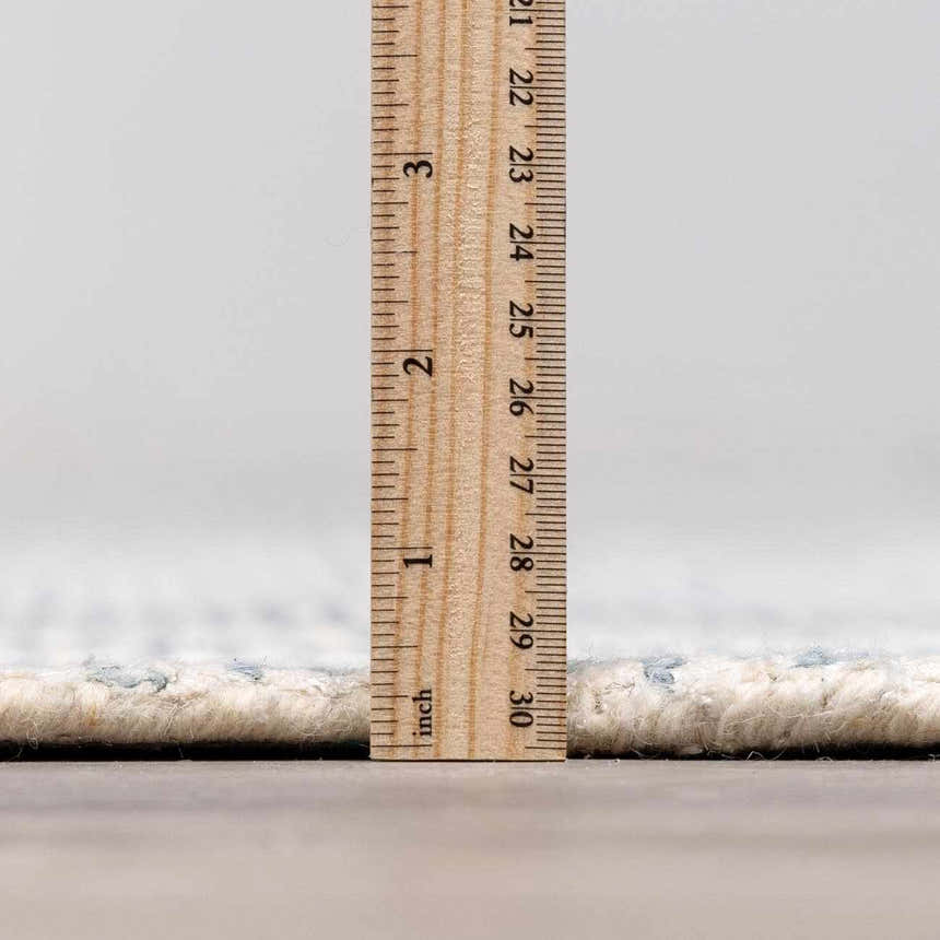 Close-up of the Orcas Hand Tufted Wool-Blend Rug in Slate, showing the pile height with a ruler. Cream and blue tones. Pile