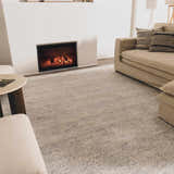 Living room scene with a slate Orcas Hand Tufted Wool-Blend Rug, beige sofa, fireplace, and neutral tones for a cozy, modern look. Roomscene-Rectangle