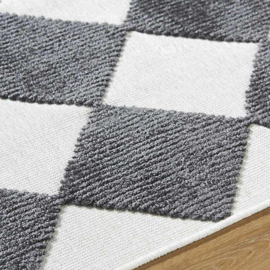Close-up of the Bosley Black Washable Area Rug. Features a black and off-white checkerboard pattern with a textured, machine-woven pile. Texture
