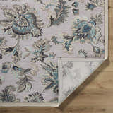 Close-up of the Benita Area Rug. Aqua, cream, and light brown floral pattern on a tan background. Machine woven texture. Fold