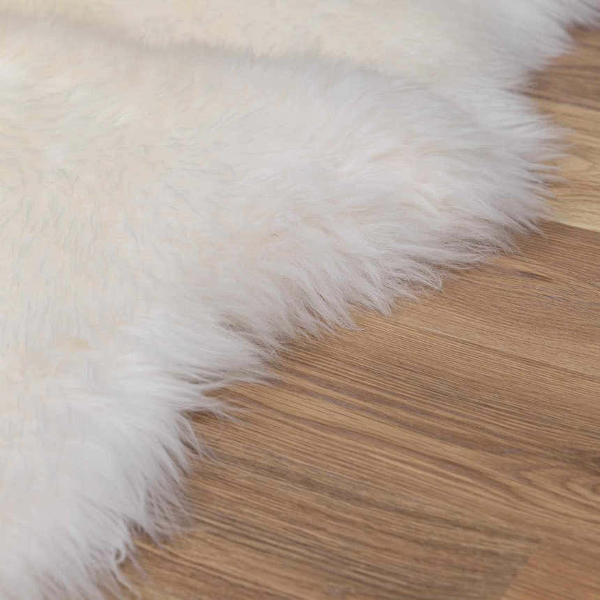 Close-up of a Premium White Soft Sheepskin Rug showing the ivory color and soft, shaggy texture on wood floor. Texture