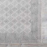 Close-up of the Brushton Area Rug. Beige cotton rug with black geometric diamond and border patterns, and fringe. Swatch