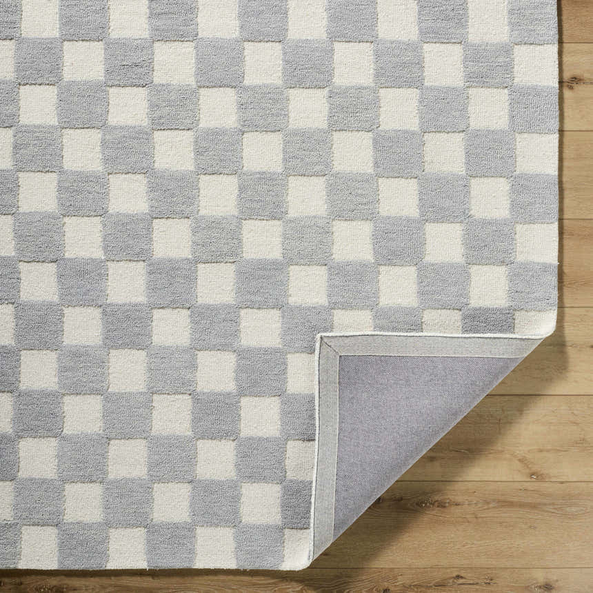 Close-up of the Amparo Medium Gray Area Rug, a hand-tufted wool rug with an ivory and medium gray checkerboard pattern. Fold