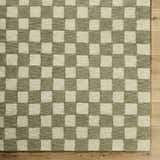 Close-up of the hand-tufted Amparo Olive Area Rug, a beige and olive wool rug with a checkerboard pattern on wood floor. Corner