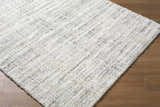 Close-up of the Yidia White Solid Area Rug. Machine woven polyester rug with off-white, light gray, and black tones. Corner