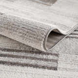 Close-up of the Bronka Broken-Striped Area Rug showing its gray, off-white, and black geometric pattern and soft texture. Fold