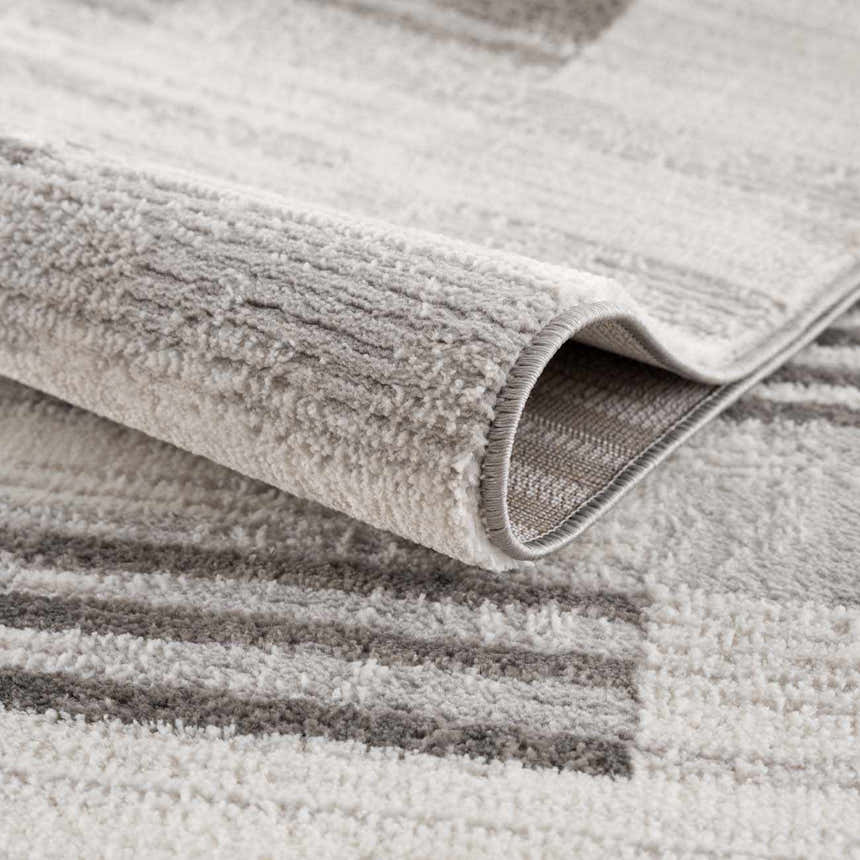 Close-up of the Bronka Broken-Striped Area Rug showing its gray, off-white, and black geometric pattern and soft texture. Fold