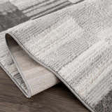 Close-up of the Bronka Broken-Striped Area Rug. Gray, off-white, and black geometric pattern with a textured, machine-woven construction. Fold