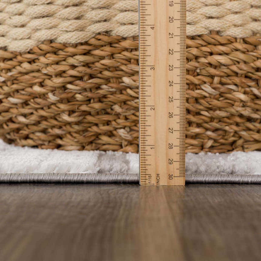 Close-up of Bronka Broken-Striped Area Rug showing rug thickness with a ruler. Colors are black, gray, and off white. Pile