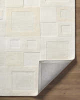 Close-up of the Botham Area Rug. Hand-tufted wool rug with geometric square design in beige, cream, and ivory tones. Fold