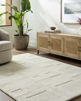 Living room scene with a beige Botham Area Rug, light wood cabinet, and potted plant. Roomscene-Rectangle