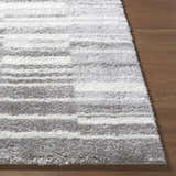Close-up of the plush Carlen Gray Area Rug showing its soft shag texture and gray and ivory stripes on wood floor. Front