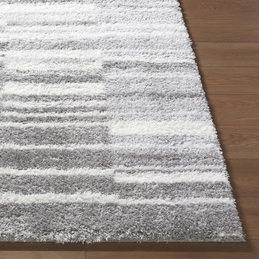 Close-up of the plush Carlen Gray Area Rug showing its soft shag texture and gray and ivory stripes on wood floor. Front
