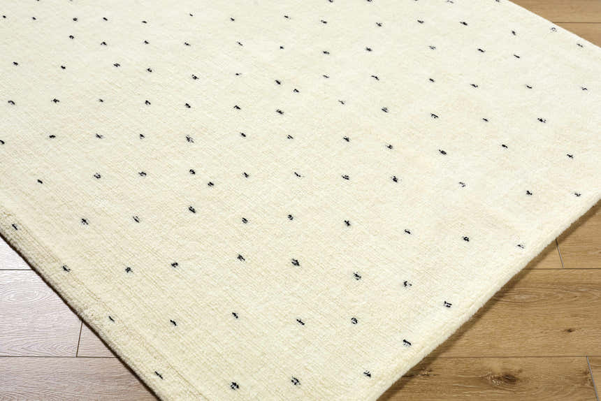 Close up of the ivory Cirila Dotted Wool Rug. Hand tufted wool rug with charcoal dots on a textured background. Corner