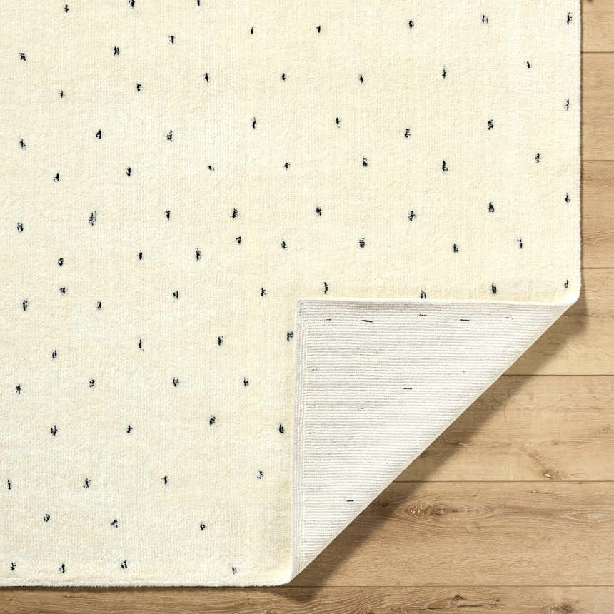 Close-up of the Cirila Dotted Ivory Washable Wool Rug. Features a dotted charcoal pattern on soft ivory wool with a hand-tufted texture. Fold