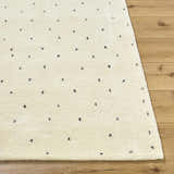 Close up of the ivory Cirila Dotted Wool Rug showing wool texture and charcoal dots on a wood floor. Front