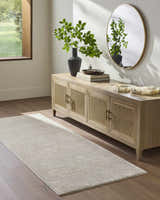 Entryway with light sage Catrin Area Rug, wood floors, and a rattan console table with a round mirror. Roomscene-Runner