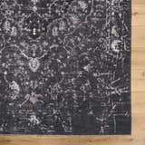 Close-up of the Corina Black Area Rug showing its traditional floral pattern and distressed texture on a light wood floor. Corner