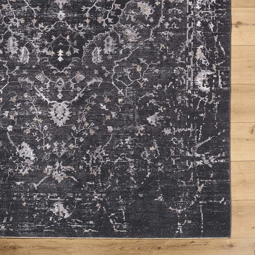 Close-up of the Corina Black Area Rug showing its traditional floral pattern and distressed texture on a light wood floor. Corner