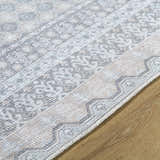 Close-up of Rainier rug showing traditional pattern in green, olive, pale blue, and white on wood floor. Texture