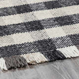 Close-up of the hand-woven Chilliwack Gray Plaid Wool Rug showing its charcoal, cream, and gray tones and textured fringe. Pile