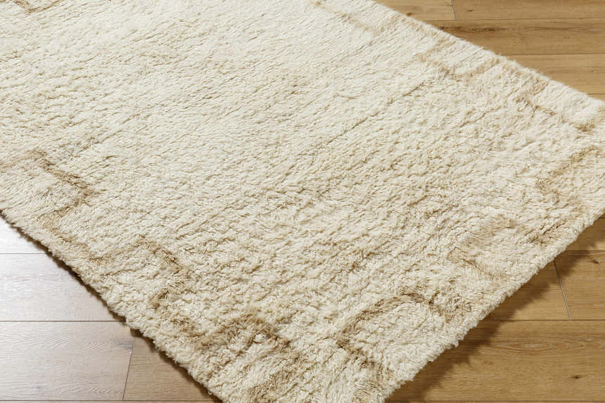 Close-up of the Ciniod Area Rug. Hand-tufted 100% wool rug in pearl and tan with a subtle pattern. Soft texture. Corner