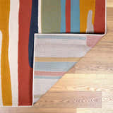 Close-up of the New Southfields Area Rug showing its abstract design, aqua, charcoal, and mustard colors, and woven backing. Fold