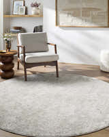 Living room scene with a round Carlyn Area Rug in cream, light sage, and light slate under a chair. Roomscene-Round