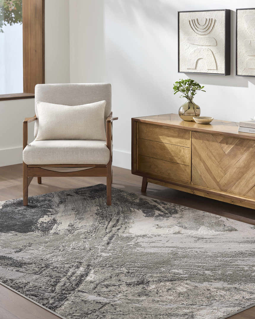 Living room scene with a beige armchair and the abstract Chaeli Area Rug in beige, black, and charcoal. Roomscene-Rectangle