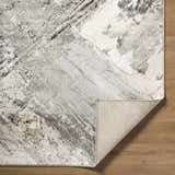 Close-up of the Chaeli Area Rug showing its beige, black, charcoal, and ivory abstract pattern and machine-woven texture. Fold