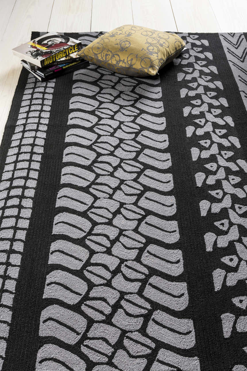 Close-up of the black and gray Cressona Area Rug with a tire track design, styled with books and a pillow. Styleshot