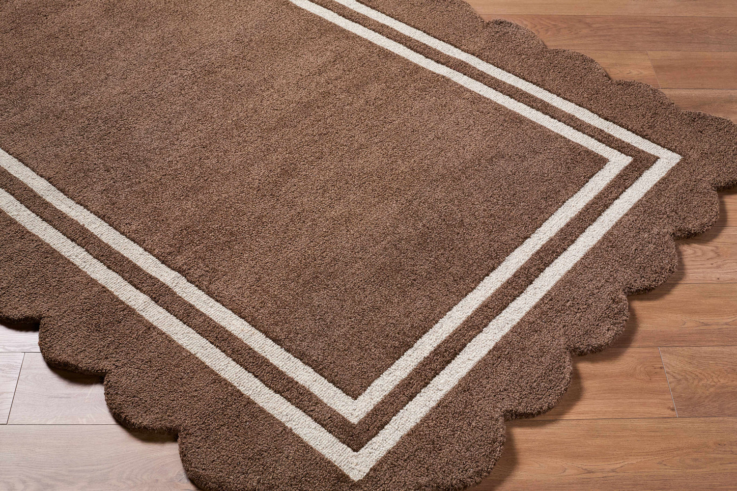 Close-up of a hand-tufted Chogan Chocolate Brown Area Rug. The wool rug has a scalloped edge and a double stripe border. Corner