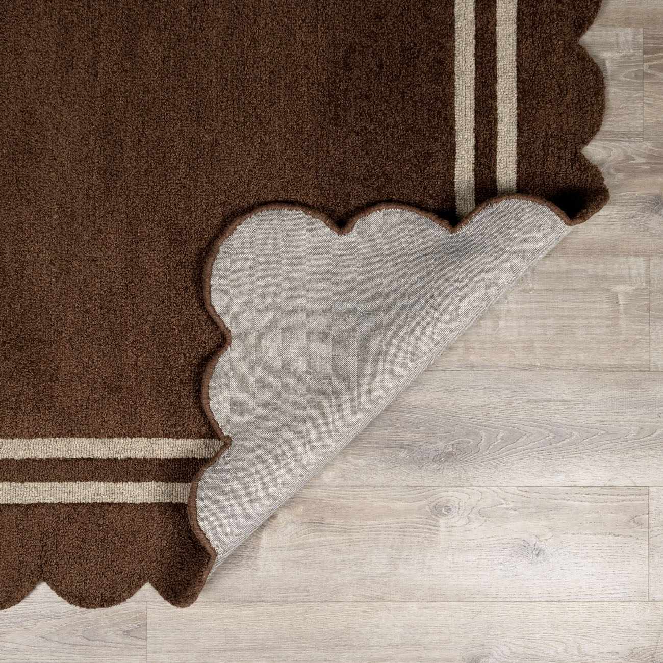 Close-up of the hand-tufted Chogan Chocolate Brown Area Rug with a scalloped edge and two beige stripes. Wool texture. Fold