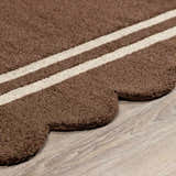 Close-up of the hand-tufted Chogan Chocolate Brown Area Rug, featuring a scalloped edge and cream stripes on a wool texture. Pile