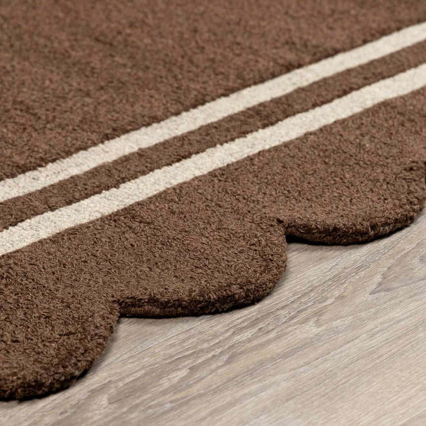 Close-up of the hand-tufted Chogan Chocolate Brown Area Rug, featuring a scalloped edge and cream stripes on a wool texture. Pile