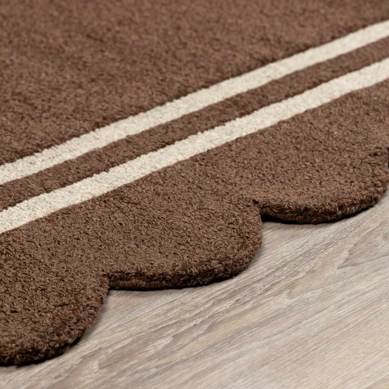 Close-up of the hand-tufted Chogan Chocolate Brown Area Rug, featuring a scalloped edge and cream stripes on a wool texture. Pile