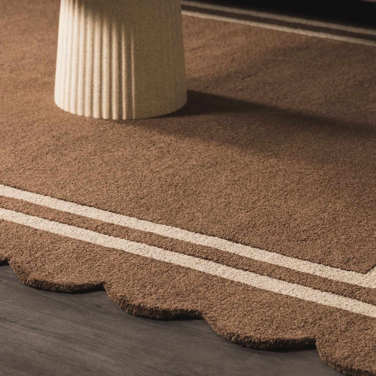 Close-up of the hand-tufted Chogan Chocolate Brown Area Rug, featuring a scalloped edge and cream-colored stripes. Roomscene-Rectangle