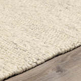 Close-up of a textured, hand-woven Clarke Textured Braided Stripe - Dark Beige Area Rug on wood floor. Pile
